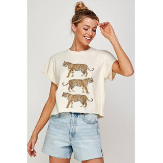 Woman wearing a cream t-shirt with tiger prints and light blue denim shorts on a plain background