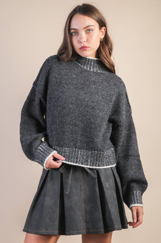 Woman wearing a gray sweater and skirt against a beige background