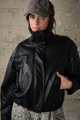 Model wearing oversized high collar faux leather zip-up jacket with leopard print skirt and embellished cap