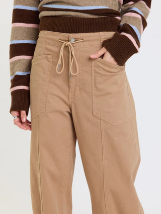 A person wearing tan wide-leg cargo-style pants with a drawstring waistband, shown from the chest down against a plain light background. The person is also wearing a brown, beige, pink, and light blue striped sweater.