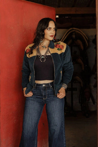 Woman wearing a stylish jacket with floral designs against a red wall.