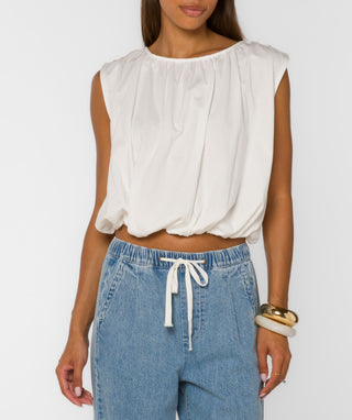Woman wearing a white sleeveless top and blue jeans on a plain background