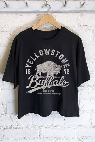 Black t-shirt with 'Yellowstone Buffalo' graphic on a hanger against a white brick wall.