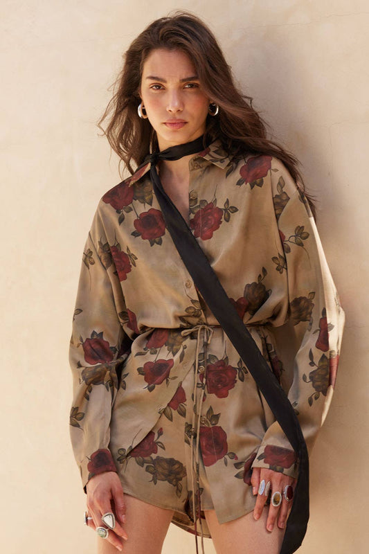 Woman wearing a floral dress with a black strap over her shoulder against a neutral background