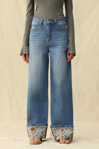 Person wearing blue jeans with floral cuffs on a beige background
