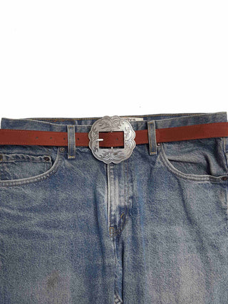 Brown leather belt with large silver engraved western floral buckle on faded blue jeans