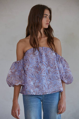 Lavender floral off-the-shoulder top with puff sleeves, paired with blue jeans.