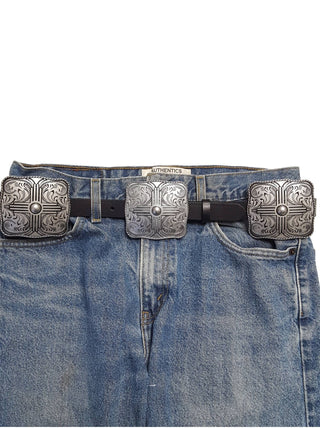 Black leather belt with three large silver engraved western concho buckles on blue jeans