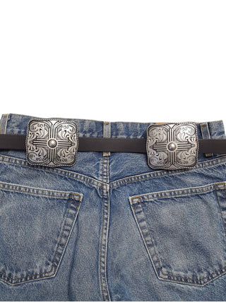 Dark brown leather belt with two square silver Western concho buckles on blue jeans