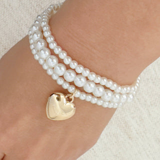 Three-strand white pearl bracelet set with gold heart charm on wrist