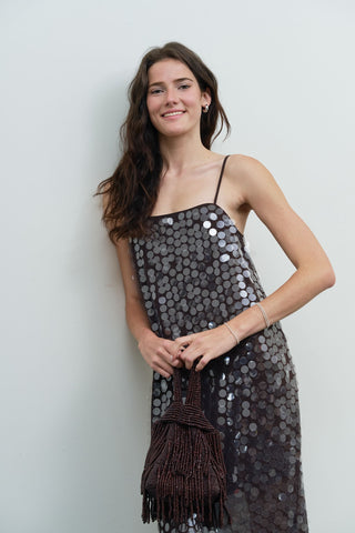 Model wearing a dark brown large-sequin spaghetti strap slip midi dress holding a beaded fringe bag