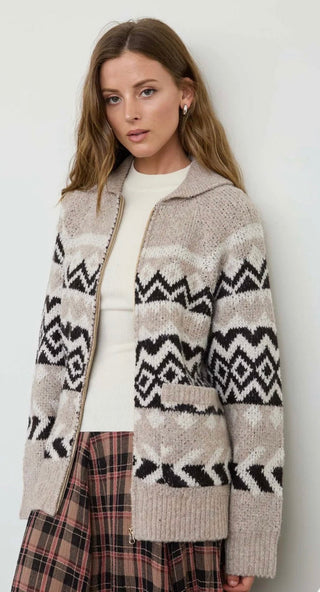 Model wearing a collared zip-up knit cardigan with geometric Fair Isle pattern over white top and plaid skirt