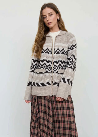 Model wearing a zip-up Fair Isle knit cardigan with geometric pattern over a plaid midi skirt