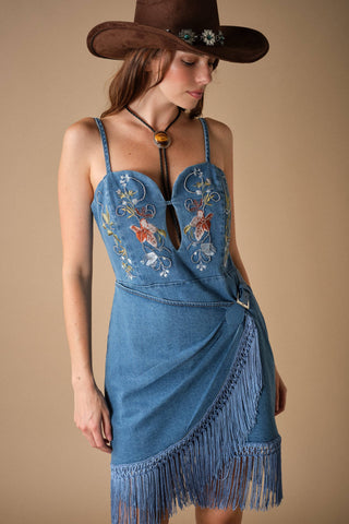 Model wearing embroidered denim mini dress with fringe hem, spaghetti straps, and keyhole bodice