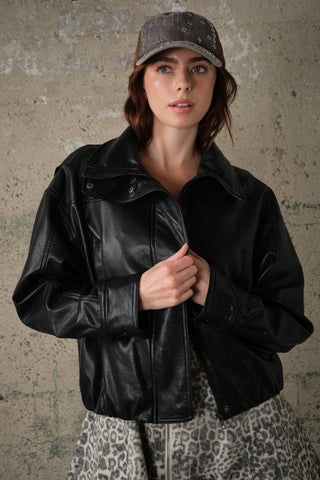Model wearing oversized faux leather jacket with high collar, paired with leopard print skirt and cap