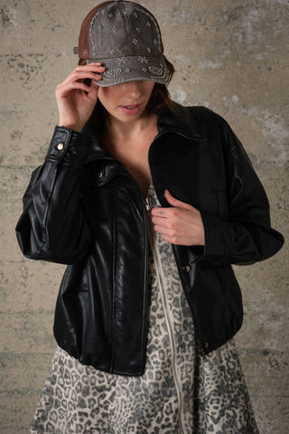 Model wearing oversized black faux leather jacket with high collar and zip closure