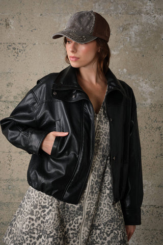 Model wearing oversized high collar faux leather jacket styled over leopard print dress with cap