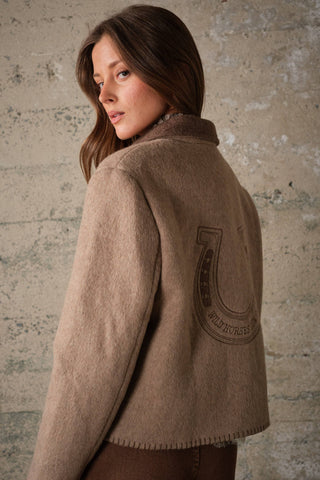 Woman wearing a wool jacket showing embroidered horseshoe graphic on the back
