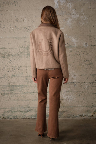 Back view of a wool jacket with horseshoe embroidery patch, worn with flared brown trousers