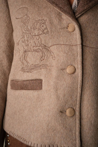 Close-up detail of wool jacket with embroidered horse and rider motif and tan buttons