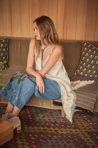 Model seated on velvet sofa wearing lace-trim satin cami with jeans and western boots