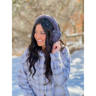 Grey faux fur earmuffs with snow dusting worn outdoors in winter setting