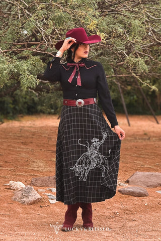 Black plaid midi skirt with white cowboy embroidery, worn with burgundy hat and boots