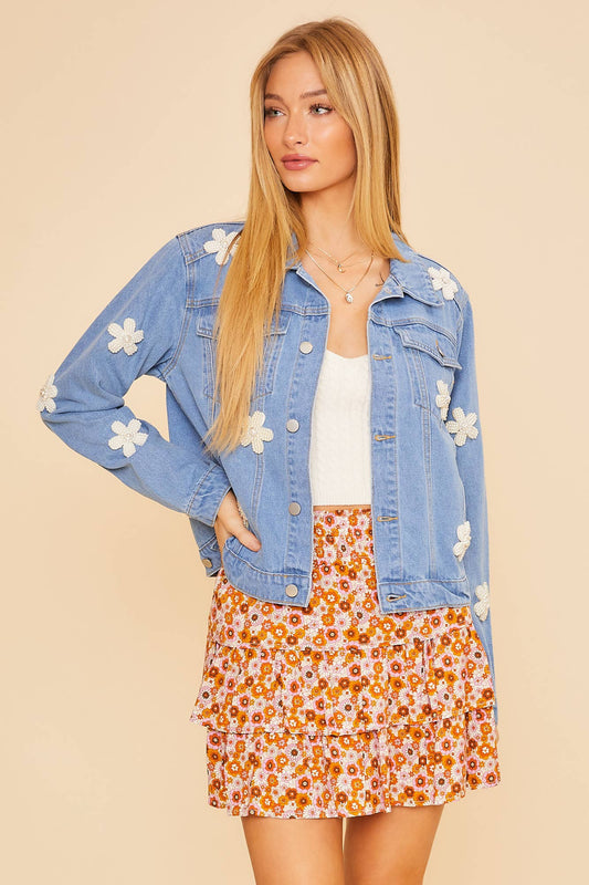 Woman wearing a denim jacket with floral patches and a floral skirt on a beige background
