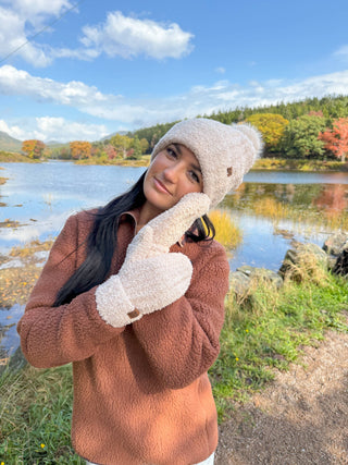 Cream textured yarn pom-pom beanie and matching mittens worn outdoors in autumn