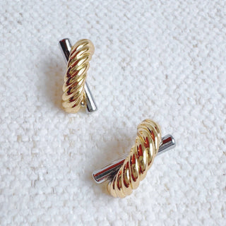 Two-tone gold and silver twisted rope crossover stud earrings on white fabric