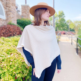 Cream and tan chevron knit poncho worn over navy long-sleeve top with wide-brim hat
