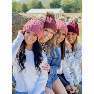 Four women wearing pink and burgundy fuzzy lined fur pom CC beanies outdoors