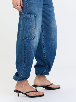 Side view of harem-style cargo denim joggers with elasticated ankles and side patch pocket