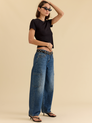 Model wearing wide-leg mid-rise cargo harem jeans with patch pocket and studded belt