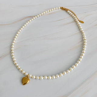 Pearl beaded necklace with gold accent beads and heart charm on marble surface