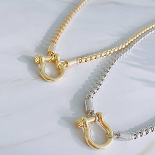 Gold and silver box chain necklaces with horseshoe shackle pendants on marble surface