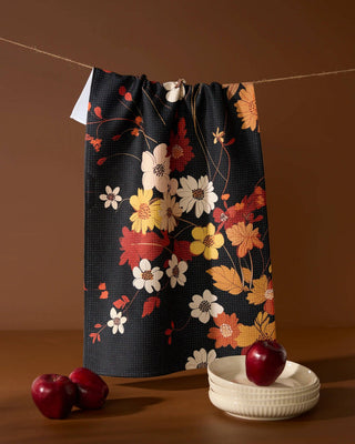 Black floral tea towel with autumn flowers in red, orange, yellow, and white