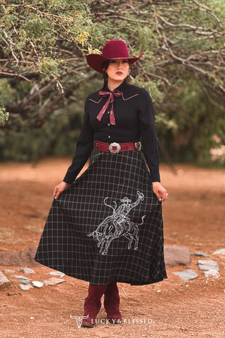 Black plaid midi skirt with white cowboy embroidery, worn with burgundy boots and hat
