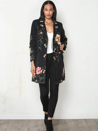 Woman wearing a black longline duster jacket with pink and orange floral embroidery over a white top and black pants