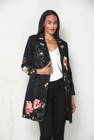 Woman wearing a black longline duster jacket with pink and green floral embroidery, open over a white top and black pants