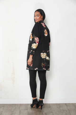 Woman wearing a black longline floral embroidered duster jacket with black leggings and ankle boots