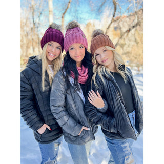 Fuzzy lined knit pom beanies in burgundy, pink, and brown worn by three women outdoors in snow
