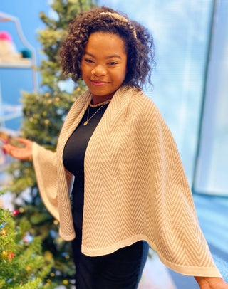 Tan herringbone knit poncho with cream border, worn over black outfit