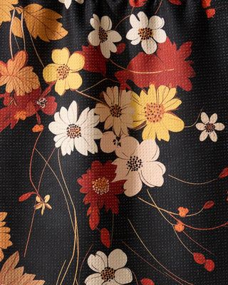 Black fabric tea towel with autumn floral print in red, yellow, and white