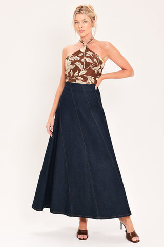 Model wearing a dark indigo denim maxi skirt with diagonal seams and flared silhouette