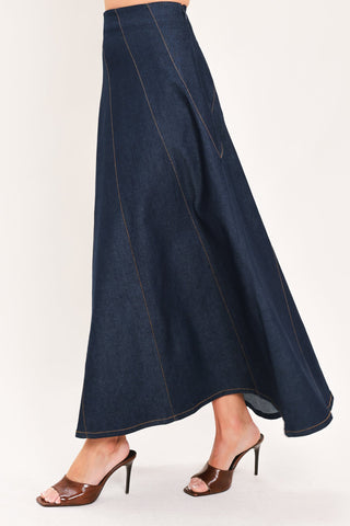 Side view of a dark denim maxi skirt with diagonal seams and flared hem on model