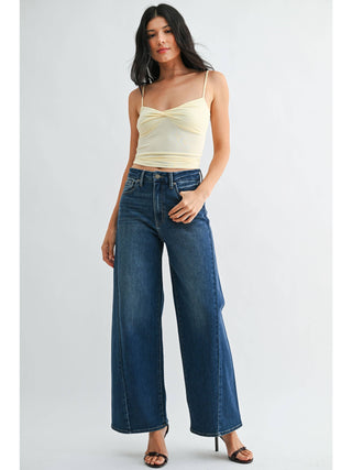 Model wearing high-rise wide leg jeans with dark wash and raw hem, styled with cream cami top