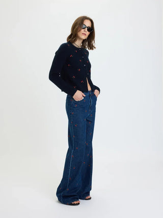 Model wearing fitted navy embroidered cardigan with cherry motifs, styled with wide-leg jeans