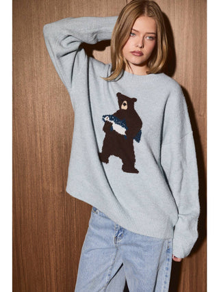 Model wearing oversized light mint crew neck sweater with large bear graphic holding a fish