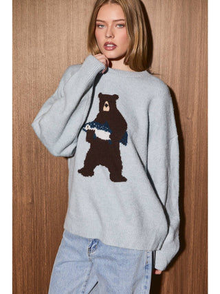 Model wearing oversized crew neck knit sweater with large bear graphic holding a fish